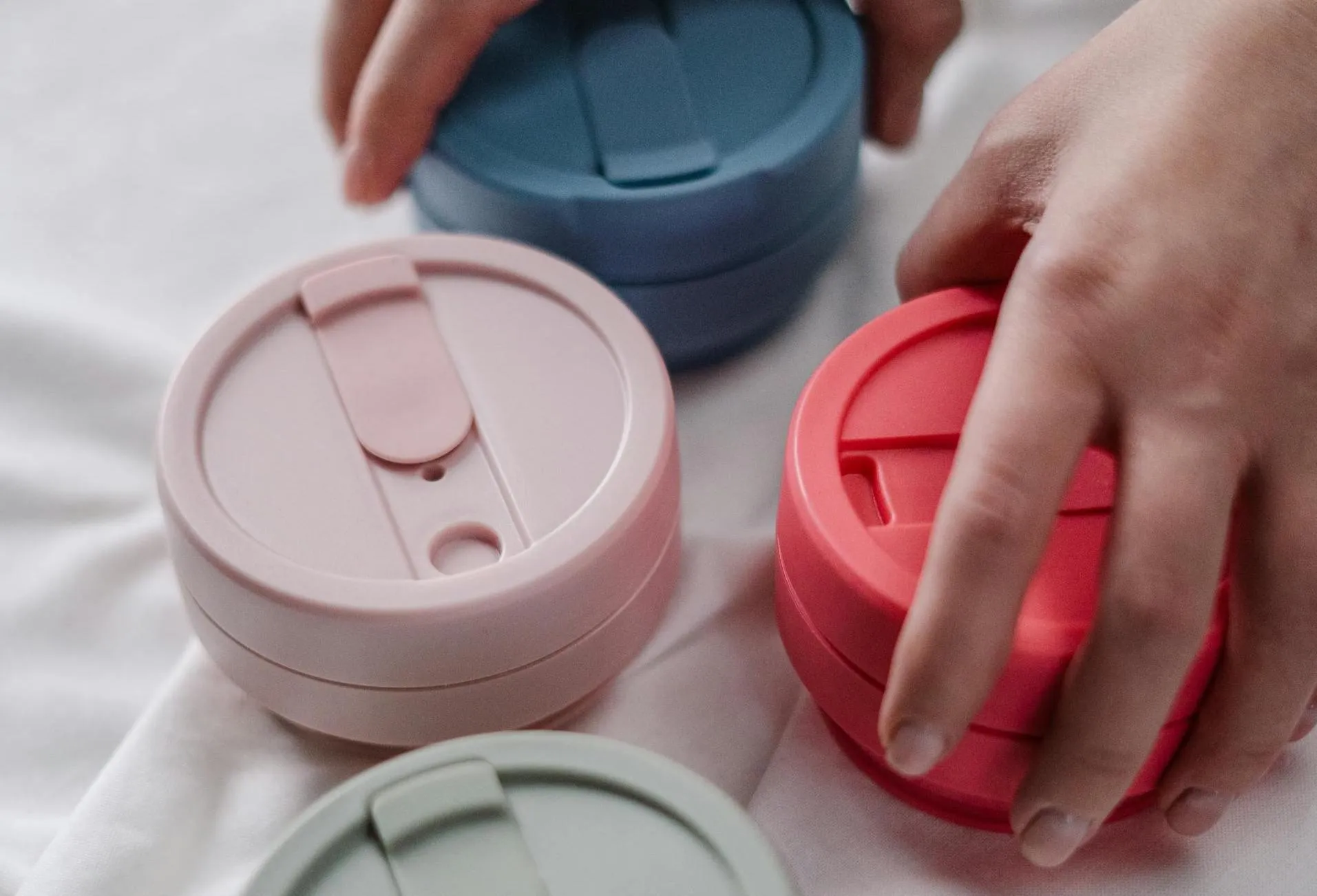 A hand reaches for a reusable mug in a selection of products.