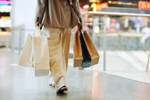 A woman in an oversized suit is seen from behind walking through a mall with a number of shopping bags.