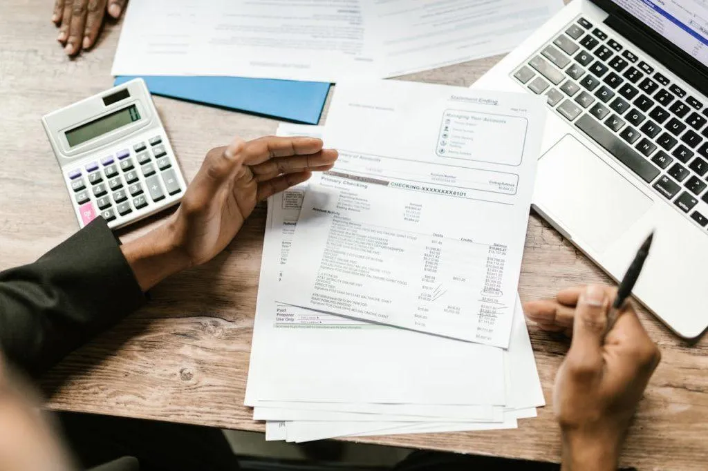 Hands resting on a wooden table over resale certificates and other documents. There is also an open laptop and a calculator.