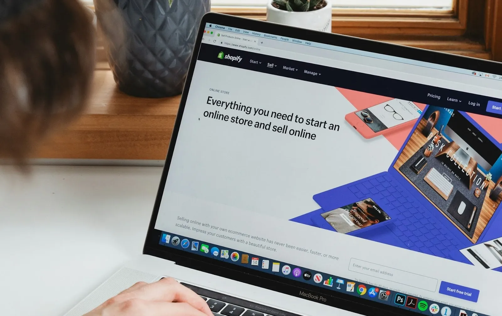 A laptop displaying shopify.com with the text ‘Everything you need to start an online store and sell online.’ A woman out of frame is working on the laptop.